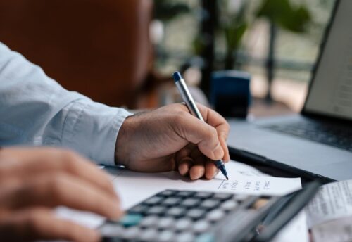 Free A person calculating finances with a calculator and pen on a desk indoors. Stock Photo