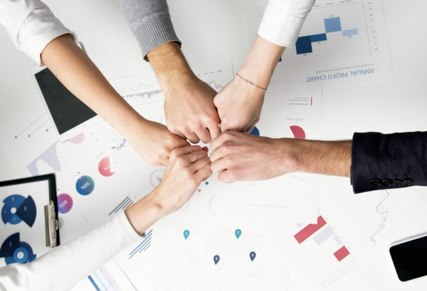 Free Colleagues celebrate success with a fist bump over financial charts depicting teamwork and unity. Stock Photo